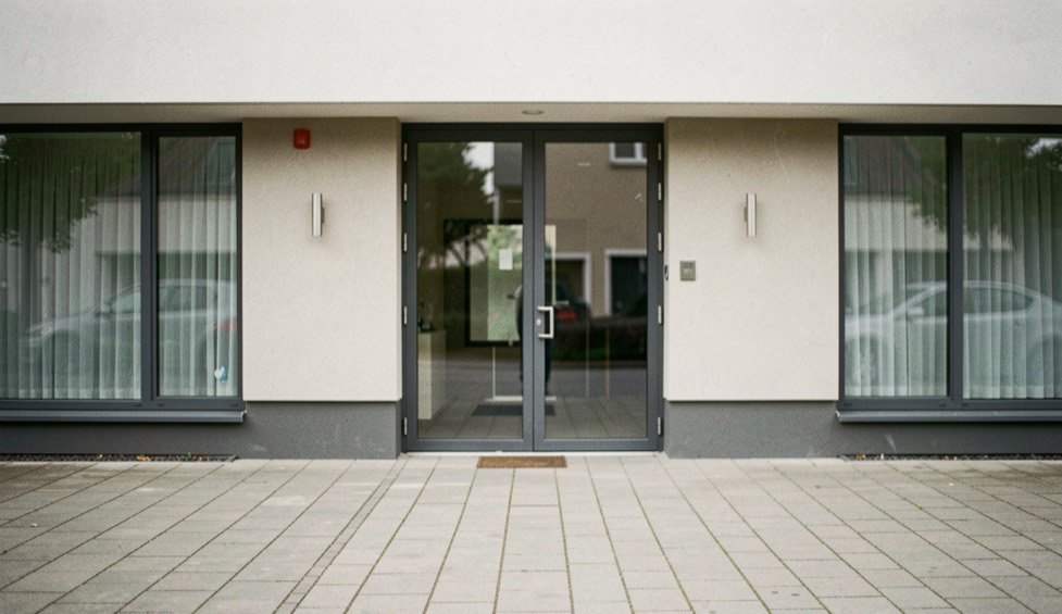A symmetrical frontal view of a modest contemporary facade, camera centered and level with paving lines meeting the building base