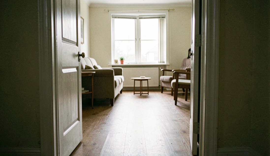 An interior photographed from a threshold so doorway, circulation route, furniture scale and far window can be read in one frame