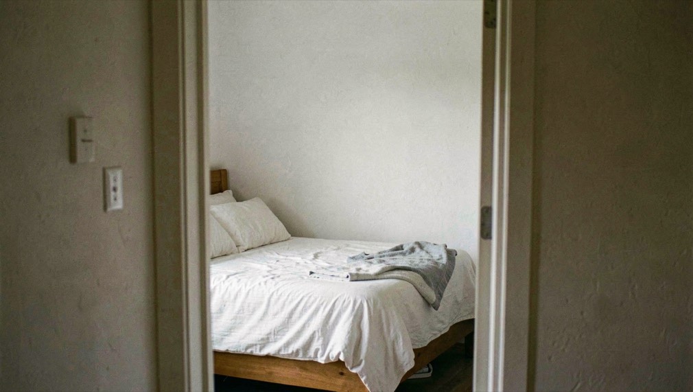 A compact bedroom photographed from just inside the doorway, believable bed proportions and straight wall edges retained without stretching